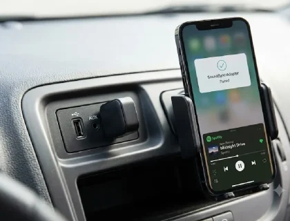 Bluetooth car adapter plugged into a car's AUX port next to a smartphone
