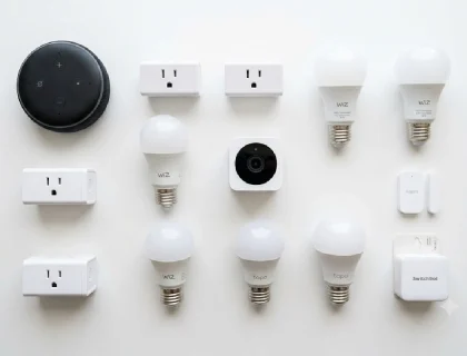 Ten budget smart home devices under $100 arranged on a white surface including Echo Dot, smart plugs, bulbs, and camera